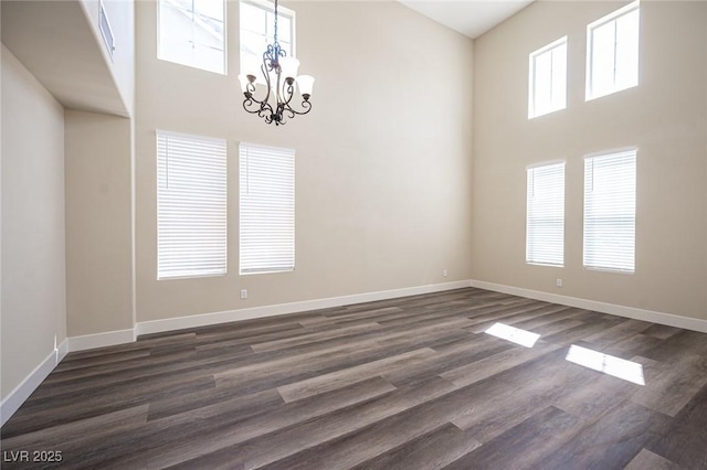 empty room with baseboards, a notable chandelier, and a towering ceiling