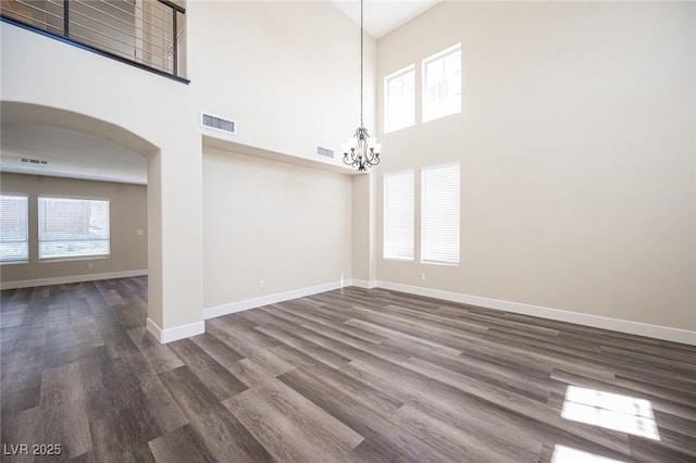 unfurnished dining area with visible vents, baseboards, arched walkways, a chandelier, and a towering ceiling
