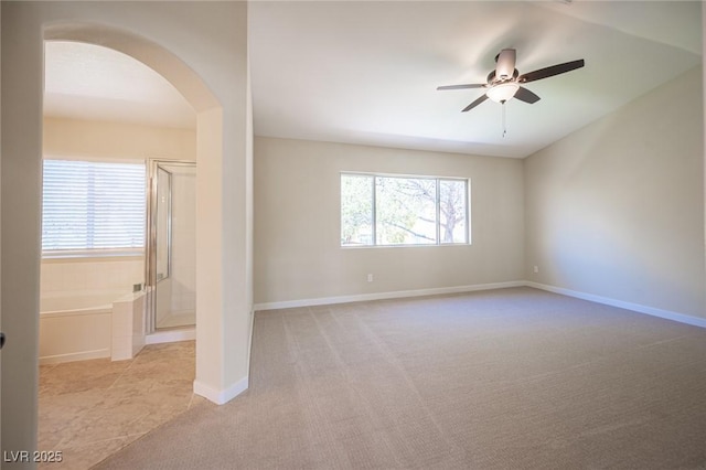 carpeted empty room featuring arched walkways, a healthy amount of sunlight, baseboards, and a ceiling fan