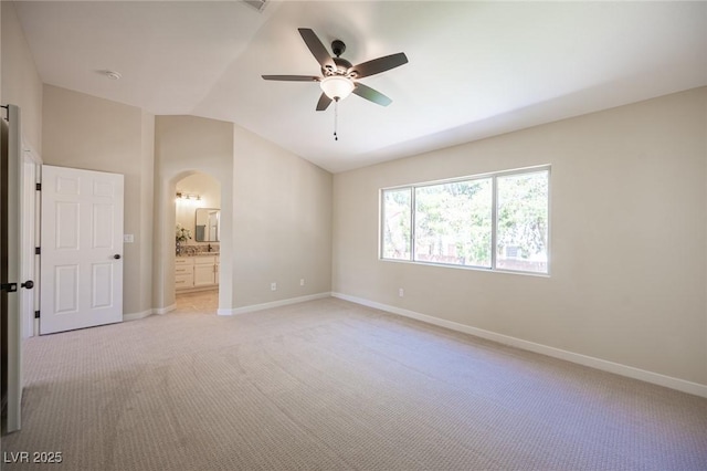 unfurnished bedroom featuring arched walkways, light colored carpet, baseboards, and lofted ceiling