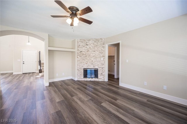 unfurnished living room featuring dark wood-type flooring, ceiling fan, arched walkways, and baseboards