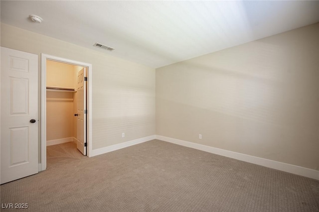 unfurnished bedroom featuring a closet, light colored carpet, a spacious closet, visible vents, and baseboards