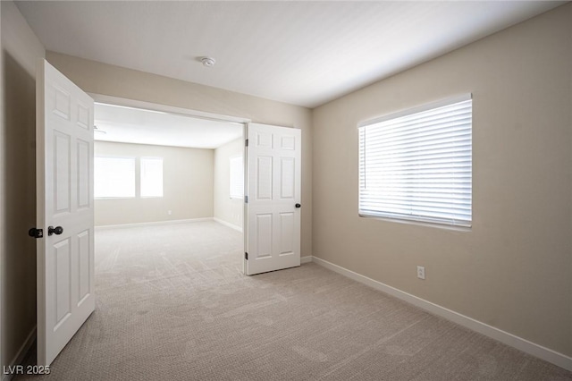 spare room with baseboards and light colored carpet