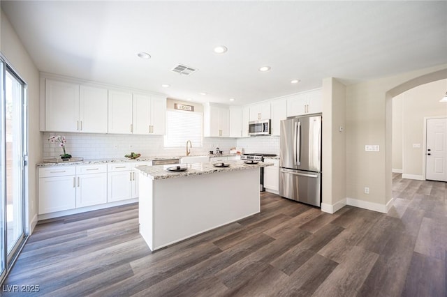 kitchen featuring visible vents, dark wood finished floors, stainless steel appliances, arched walkways, and decorative backsplash