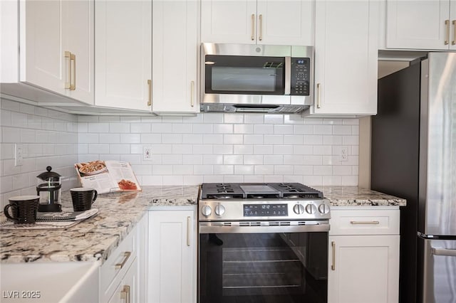 kitchen with stainless steel appliances, white cabinetry, light stone counters, and decorative backsplash