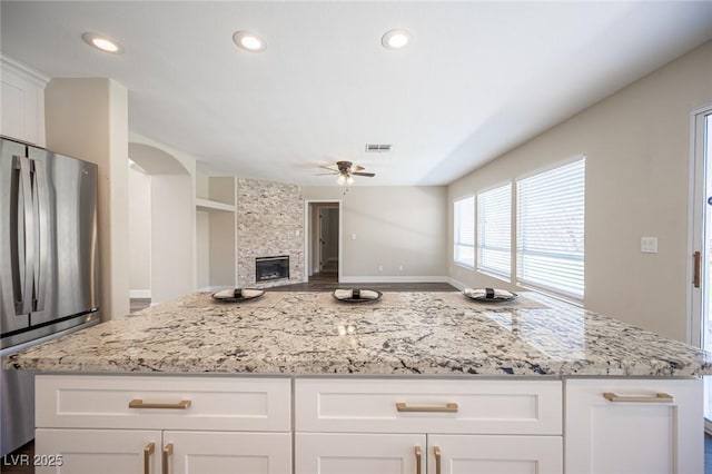 kitchen with visible vents, freestanding refrigerator, ceiling fan, and light stone countertops