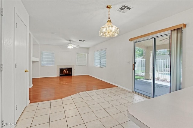 681 Peach Coral St, Las Vegas, NV 89183 - unfurnished living room with visible vents, baseboards, ceiling fan with notable chandelier, a warm lit fireplace, and light wood-style floors