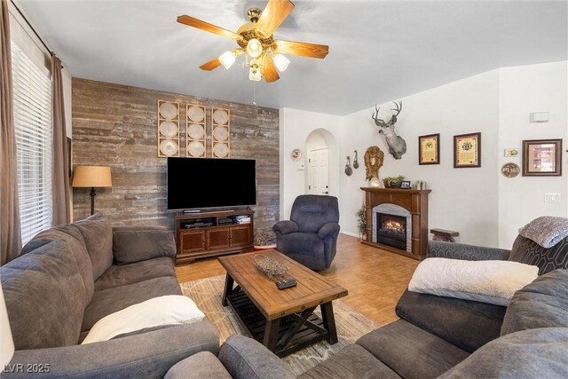 648 Sunrise Lake Pl, Henderson, NV 89002 - living area featuring arched walkways, ceiling fan, a warm lit fireplace, and wood finished floors