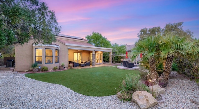9 Contra Costa Pl, Henderson, NV 89052 - back of house at dusk featuring stucco siding, solar panels, ceiling fan, an outdoor living space, and a lawn