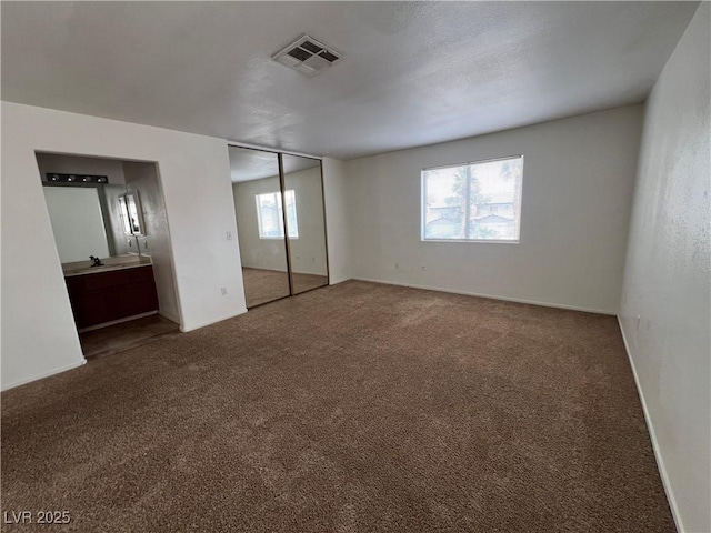 unfurnished bedroom featuring carpet flooring, a sink, visible vents, and ensuite bath