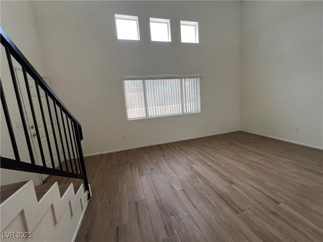 empty room featuring stairway, plenty of natural light, a towering ceiling, and wood finished floors