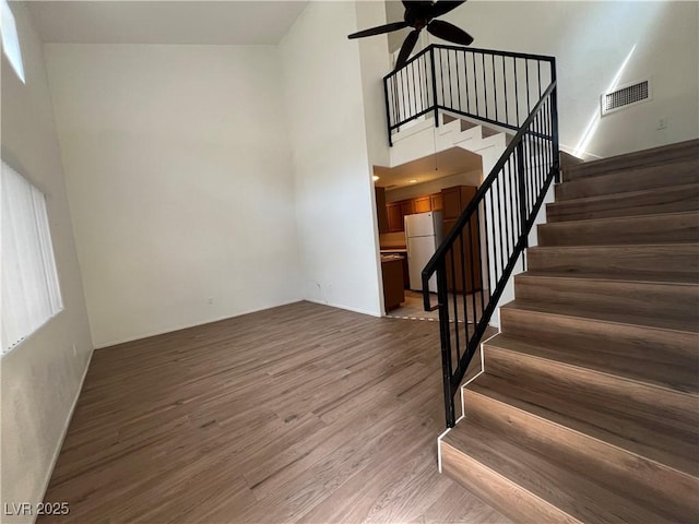 stairs with visible vents, a ceiling fan, a towering ceiling, and wood finished floors