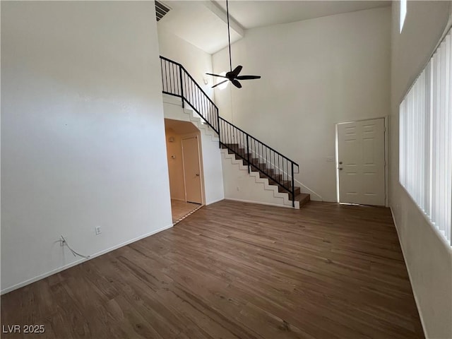 unfurnished living room featuring visible vents, a ceiling fan, a towering ceiling, wood finished floors, and stairs