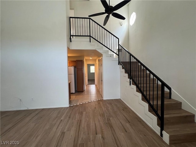 stairway featuring baseboards, a ceiling fan, a towering ceiling, and wood finished floors