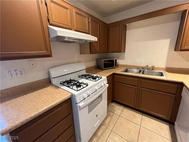 kitchen with stainless steel microwave, white range with gas cooktop, light countertops, under cabinet range hood, and a sink