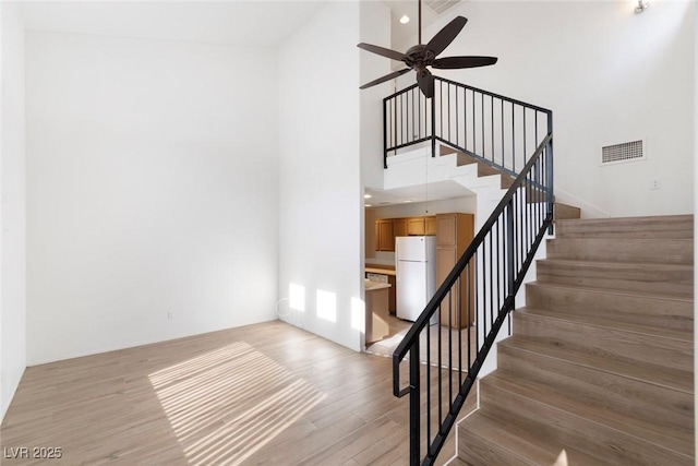 stairs with visible vents, a high ceiling, a ceiling fan, and wood finished floors