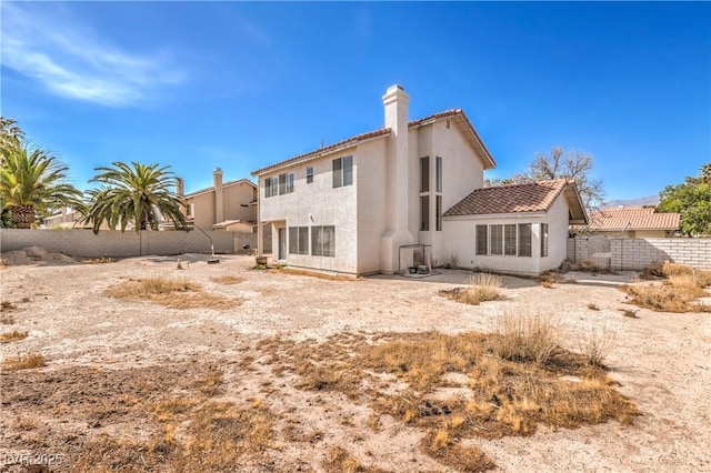 rear view of property featuring stucco siding, fence, a chimney, and a tile roof
