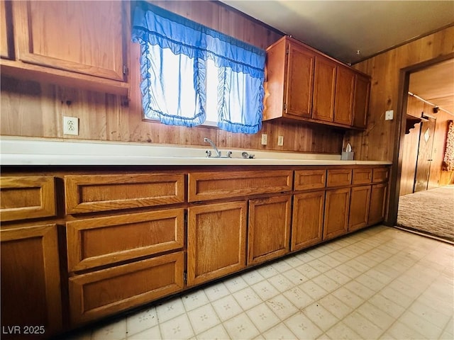 kitchen with wooden walls, light countertops, brown cabinets, light floors, and a sink