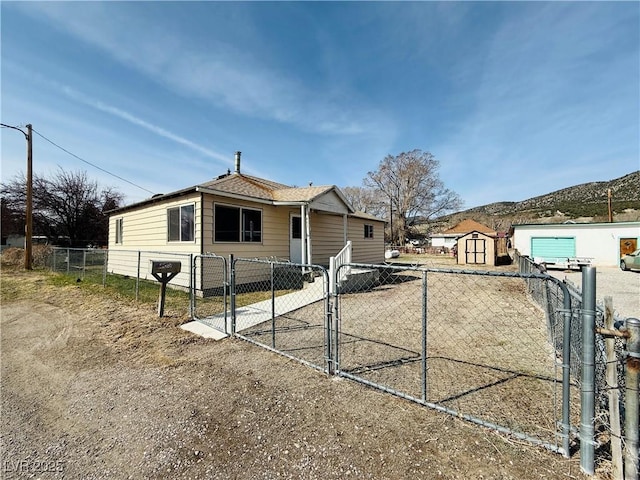 view of front facade featuring an outbuilding, fence private yard, roof with shingles, a storage unit, and a gate