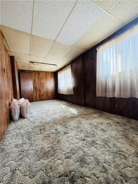 unfurnished room featuring a paneled ceiling, wood walls, and carpet floors