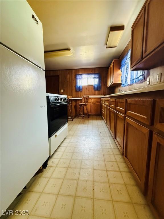 kitchen with freestanding refrigerator, light floors, brown cabinetry, wood walls, and electric range oven