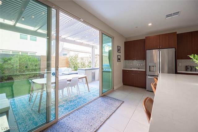 kitchen featuring visible vents, stainless steel refrigerator with ice dispenser, light tile patterned flooring, light countertops, and backsplash