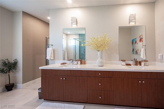 bathroom with baseboards, a sink, a shower stall, double vanity, and tile patterned floors