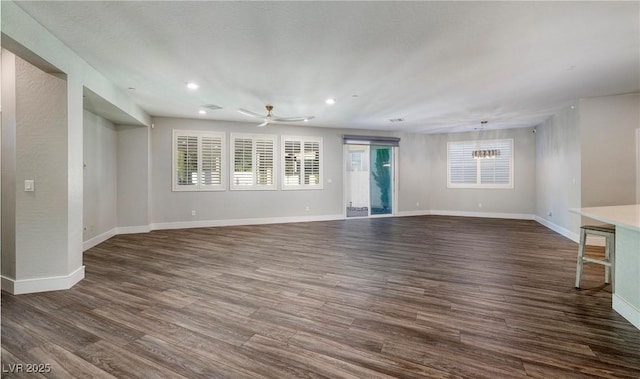 unfurnished living room with ceiling fan with notable chandelier, baseboards, dark wood finished floors, and recessed lighting