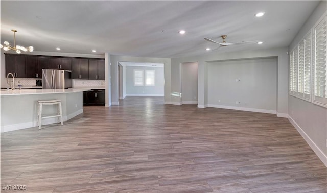 unfurnished living room with light wood-type flooring, recessed lighting, and ceiling fan with notable chandelier