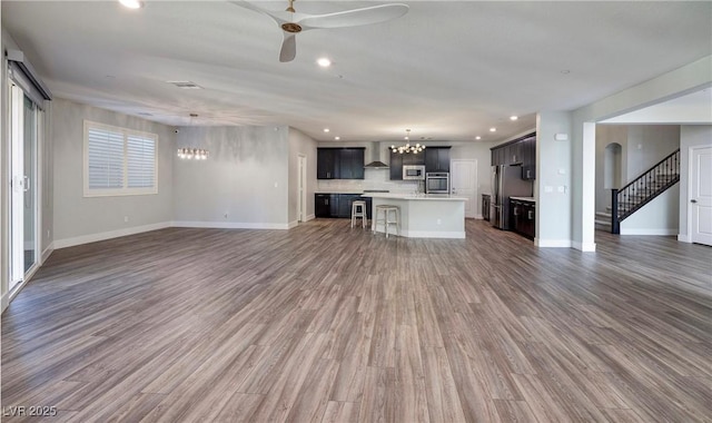unfurnished living room with recessed lighting, stairway, ceiling fan with notable chandelier, and wood finished floors
