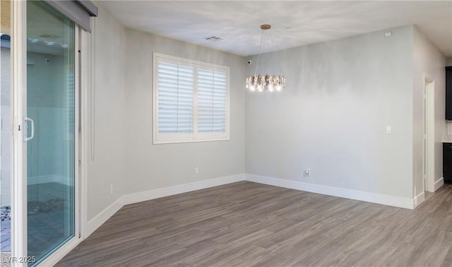 unfurnished room with wood finished floors, an inviting chandelier, and baseboards