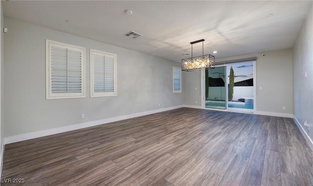 empty room with an inviting chandelier, visible vents, dark wood-style flooring, and baseboards