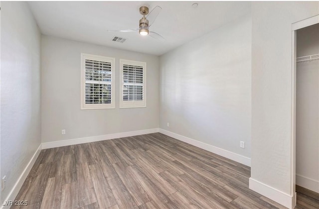 spare room with wood finished floors, ceiling fan, baseboards, and visible vents