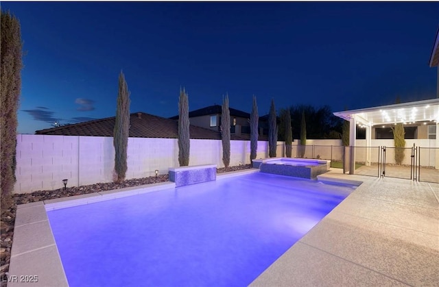 pool at night with a patio, a fenced backyard, and a pool with connected hot tub