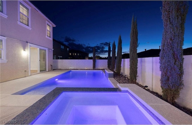 pool at night featuring a fenced backyard, an in ground hot tub, and a fenced in pool