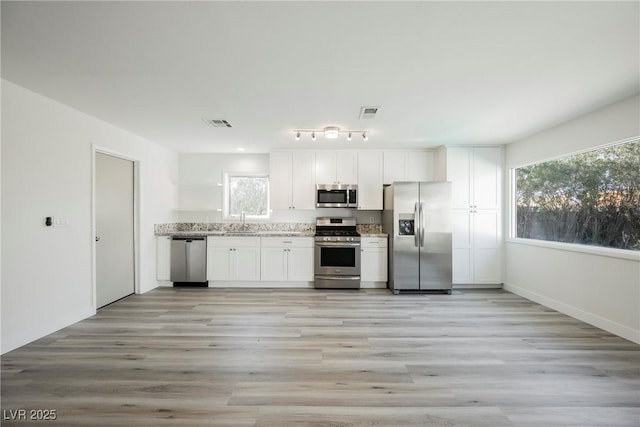 kitchen featuring light stone counters, a sink, white cabinetry, light wood-style floors, and stainless steel appliances