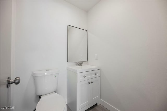 half bathroom featuring baseboards, vanity, toilet, and wood finished floors