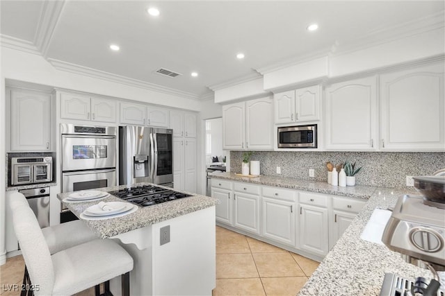 kitchen with a center island, stainless steel appliances, a kitchen breakfast bar, visible vents, and backsplash
