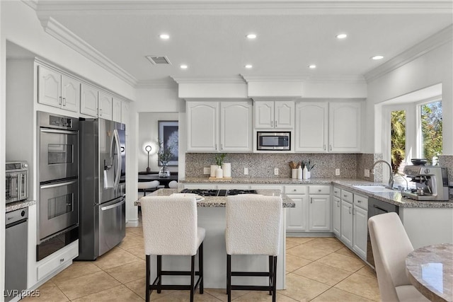 kitchen featuring light stone counters, visible vents, a sink, stainless steel appliances, and white cabinets