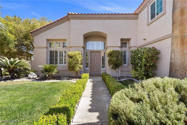 property entrance featuring a lawn, stucco siding, and a tiled roof