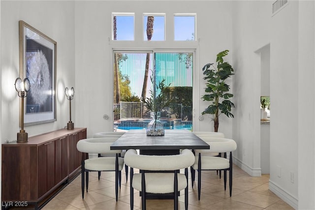 dining area with light tile patterned floors, visible vents, baseboards, and a towering ceiling