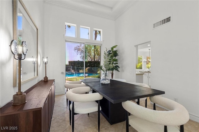 dining area with baseboards, ornamental molding, light tile patterned flooring, visible vents, and a high ceiling