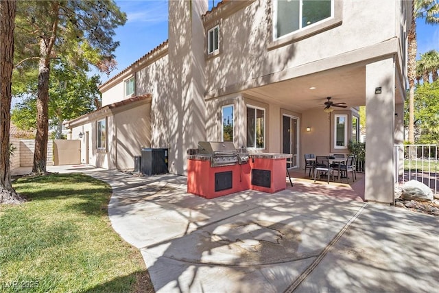 rear view of house featuring a ceiling fan, exterior kitchen, fence, a patio area, and stucco siding