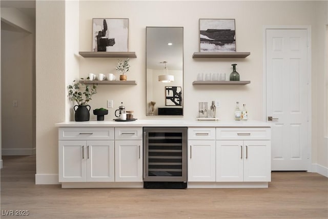 indoor wet bar featuring wine cooler, baseboards, and light wood-style flooring