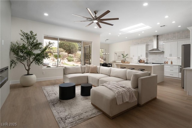 living room featuring a ceiling fan, light wood-style floors, recessed lighting, and baseboards
