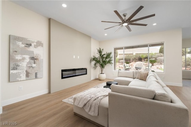 living area featuring ceiling fan, wood finished floors, a glass covered fireplace, recessed lighting, and baseboards