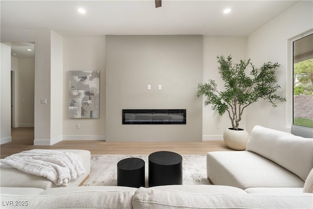 living room featuring a glass covered fireplace, wood finished floors, recessed lighting, and baseboards
