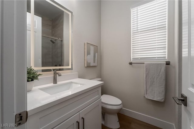 bathroom with a shower with shower door, toilet, vanity, wood finished floors, and baseboards