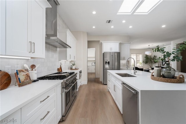 kitchen with stainless steel appliances, a sink, wall chimney exhaust hood, light wood-style flooring, and light countertops