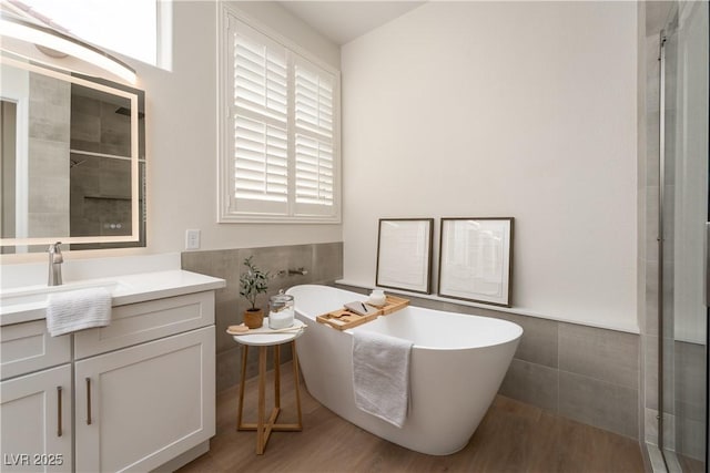 full bathroom featuring tile walls, vanity, a wainscoted wall, a freestanding bath, and wood finished floors